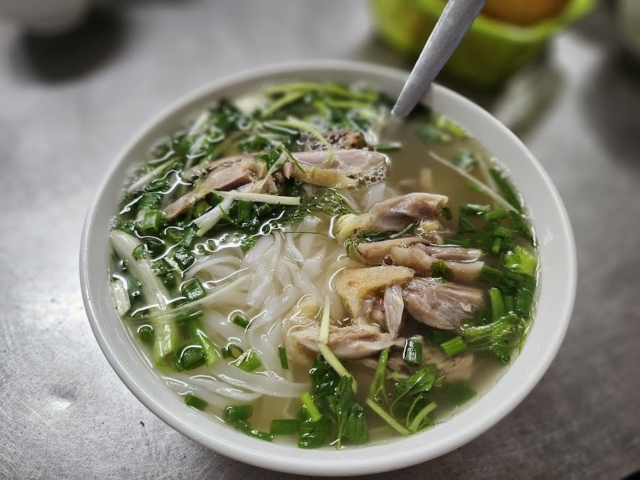 A bowl of phở gà with shredded chicken, fresh herbs, and clear broth