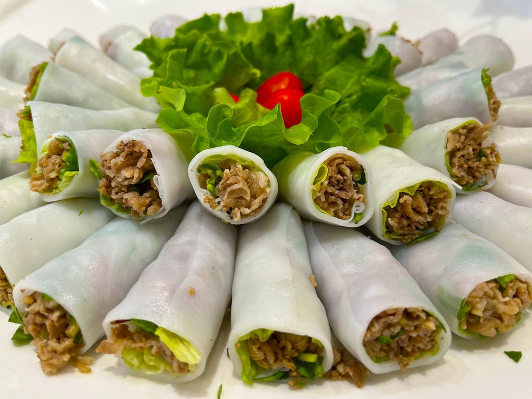 A close-up of rice noodle sheets being filled with beef and herbs for phở cuốn